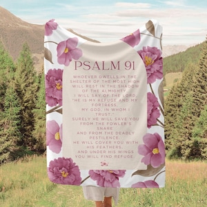 May include: A white throw blanket featuring pink floral designs and the text "PSALM 91" in a brown font. The text includes a passage from the Bible about finding refuge in God.