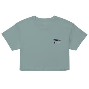 Könnte beinhalten: Hellblaues, kurzes T-Shirt mit einer kleinen Stickerei eines Formel-1-Rennwagens in Rot, Blau und Gelb. Der Text "IVER" ist darunter gestickt. Das Shirt hat kurze Ärmel und einen Rundhalsausschnitt.