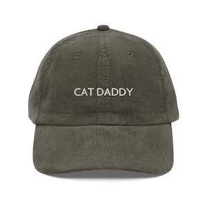 May include: A green corduroy baseball cap with the text "CAT DADDY" embroidered in white on the front.