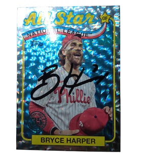 May include: A baseball card featuring Bryce Harper of the Philadelphia Phillies. The card has a holographic background with the words "All Star of National League" at the top. Harper is wearing a red Phillies cap and uniform.