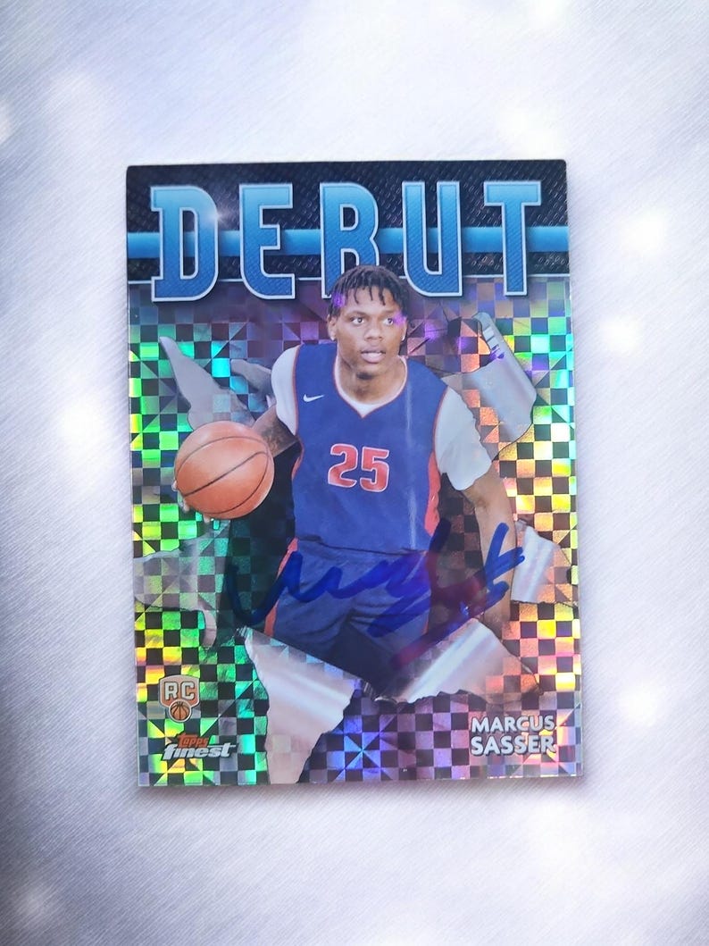 May include: A basketball trading card featuring a player in a blue and orange jersey with the number 25. The card has the word "DEBUT" at the top and the player's name, Marcus Sasser, at the bottom. The background has a holographic design.