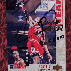 Könnte beinhalten: Basketball-Sammelkarte mit Scottie Pippen in roter Chicago Bulls-Uniform, mitten im Dunk. Die Karte enthält ein Autogramm und den Text "FIRST TEAM" und "NBA". Ein kleineres Bild von Pippen befindet sich in der unteren linken Ecke.