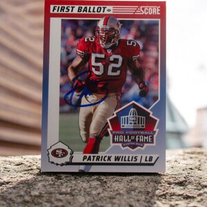 May include: A football trading card featuring Patrick Willis in a red and gold uniform with the number 52. The card includes the text "FIRST BALLOT SCORE" and "PRO FOOTBALL HALL OF FAME". The card is signed.