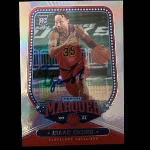 Peut inclure: Une carte de collection de basketball argentée et rouge mettant en vedette Isaac Okoro des Cleveland Cavaliers. La carte a une finition holographique et présente une photo d'Okoro dribblant le ballon. La carte est de la série Panini Marqueee 2020-21.