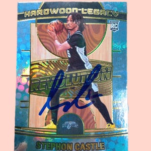 May include: A basketball trading card featuring Stephon Castle in a San Antonio Spurs uniform. The card has a holographic background with the words "HARDWOOD LEGACY" and "REVOLUTION". The card is signed with a blue marker and has the text "ROOKIE RC CARD".