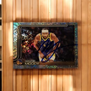 Peut inclure: Carte de collection de basket-ball avec Moses Moody en uniforme des Golden State Warriors. La carte a une bordure argentée et un design holographique. La signature du joueur est visible. Fond en bois.