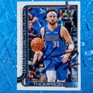 Peut inclure: Une carte de collection de basket-ball Topps représentant Klay Thompson dans un maillot bleu des Dallas Mavericks avec le numéro 31, tenant un ballon. La carte inclut un autographe à l'encre foncée, le texte MAVERICKS et son nom.