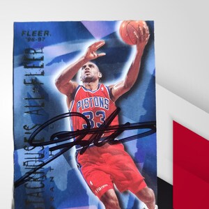 Puede incluir: Tarjeta de baloncesto coleccionable con un jugador con el uniforme rojo de los Detroit Pistons, número 33. La tarjeta tiene un fondo azul con el texto "STACKHOUSE ALL-FILLER" y "FLEER '96-'97". La tarjeta está firmada con rotulador negro.