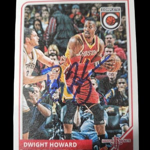 Peut inclure: Une carte de basketball blanche avec un logo Houston Rockets rouge, blanc et bleu. La carte présente une photo de Dwight Howard portant un maillot rouge et blanc avec le mot "Houston" sur le devant. La carte est signée à l'encre bleue. La carte fait partie d'un ensemble complet.