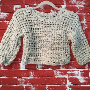May include: A cream-coloured crocheted sweater with a loose, open weave and colourful flecks throughout. The sweater has long sleeves and a round neckline.