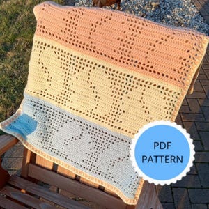 Puede incluir: Una manta de ganchillo hecha a mano en colores pastel. La manta presenta un esquema de color melocotón, crema y azul claro con un patrón calado repetido. La manta está sobre una silla de madera. Un círculo azul con el texto "PDF PATTERN" está en la imagen.
