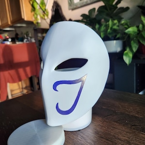 May include: A white mask with a blue 'J' design. The mask is sitting on a white base.
