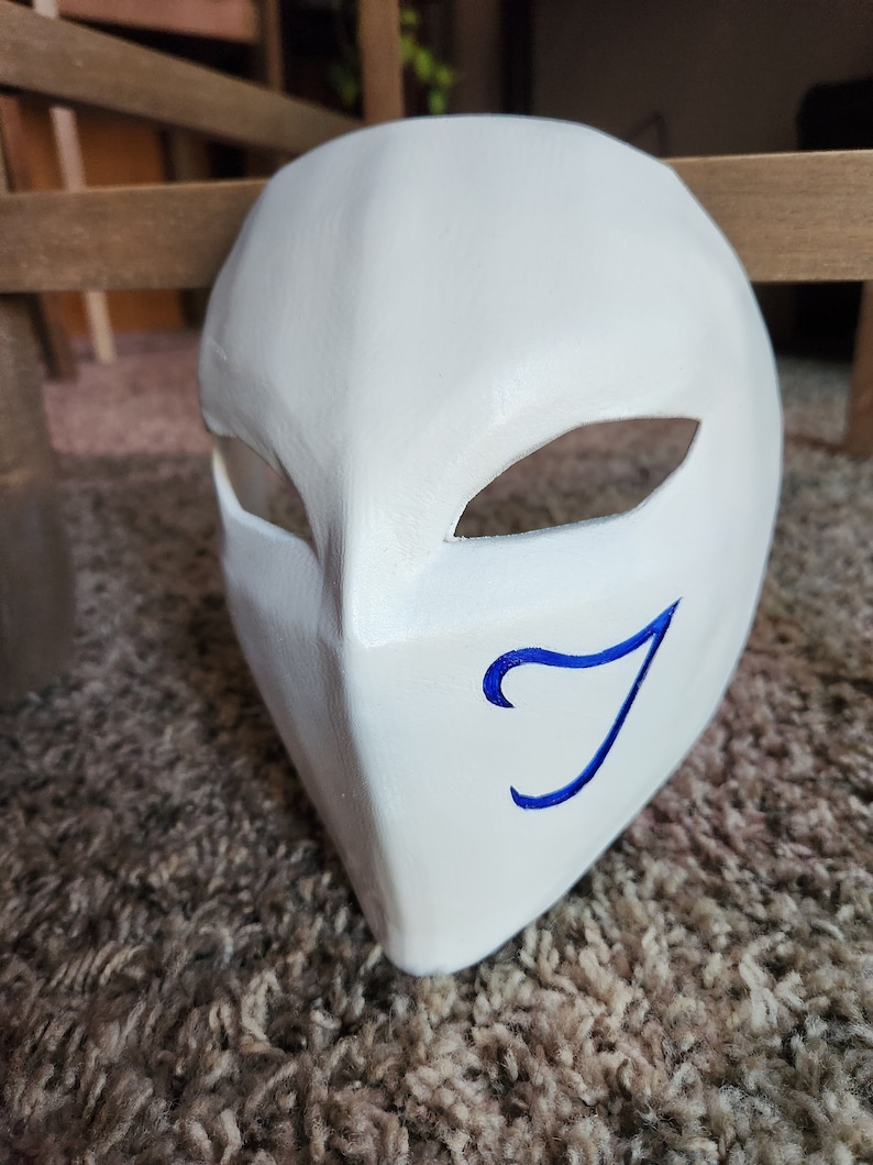 May include: White mask with a blue swirl design. The mask has two eye holes and a curved shape.