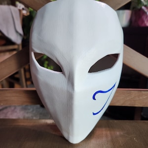 May include: White mask with a blue swirl design on the right side. The mask has two eye holes and a pointed chin.
