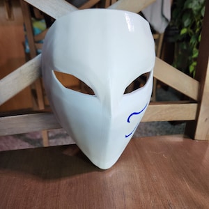 May include: A white mask with blue markings around the eyes and mouth. The mask is made of a smooth, hard material and has a glossy finish.