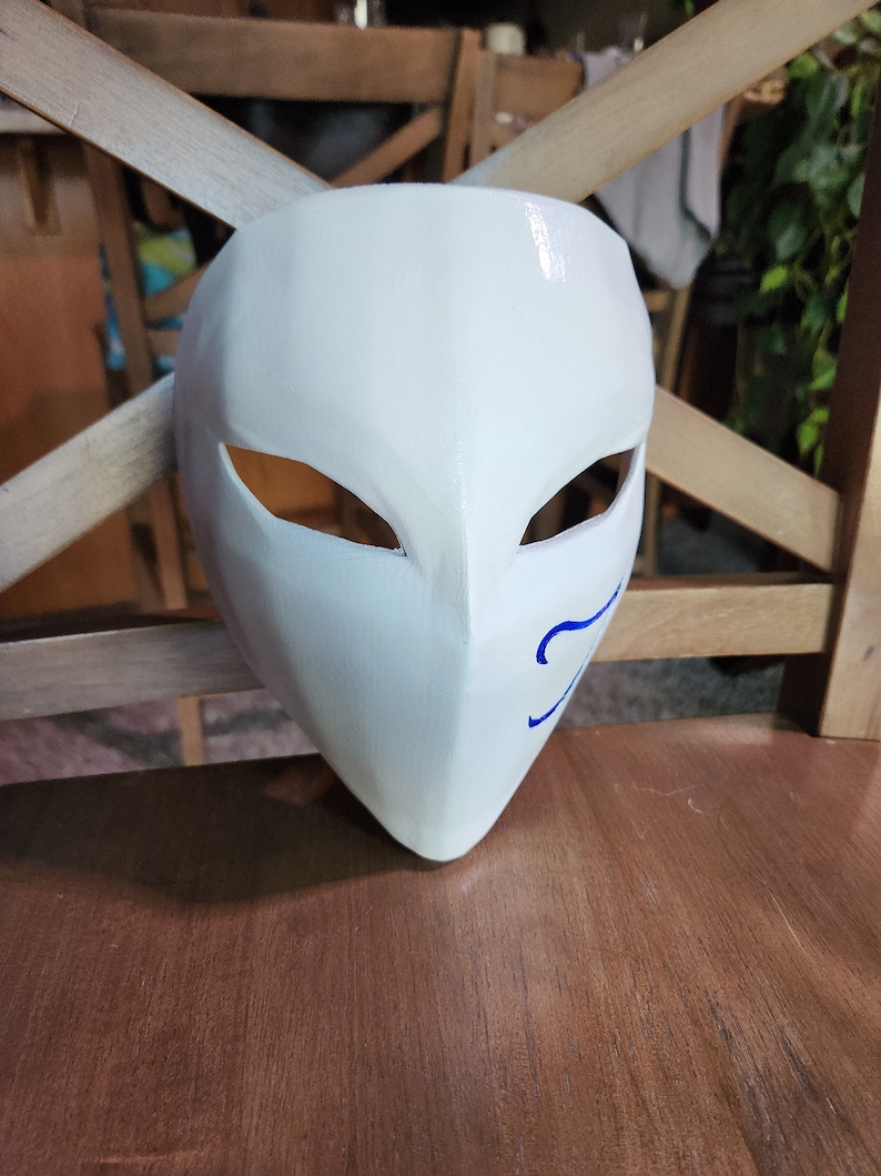 May include: A white mask with blue markings around the eyes and mouth. The mask is made of a smooth, hard material and has a glossy finish.