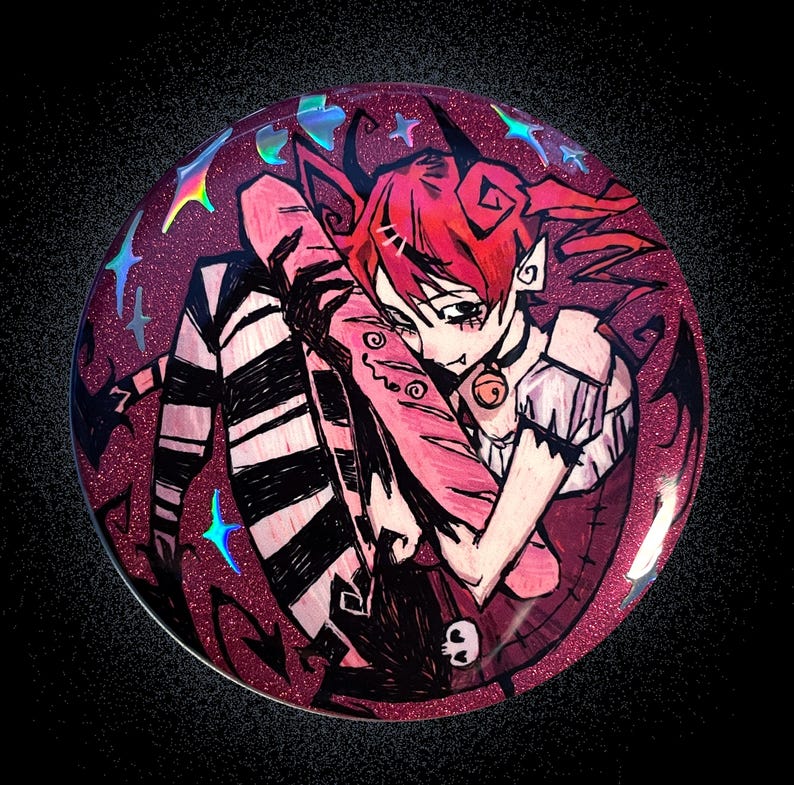 May include: A circular pin featuring a glittery magenta background with a stylized illustration of a character with red hair, black and white striped stockings, and a small bell collar, surrounded by holographic blue star accents.