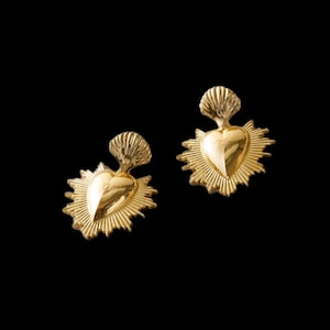 May include: A pair of gold-tone earrings featuring a heart-shaped design with a sunburst halo and a scallop shell detail.
