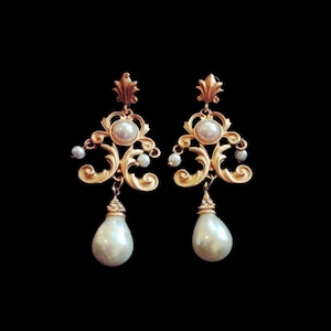 Puede incluir: Pendientes de tono dorado con un diseño barroco y detalles de perlas. Los pendientes presentan una gran gota de perla.