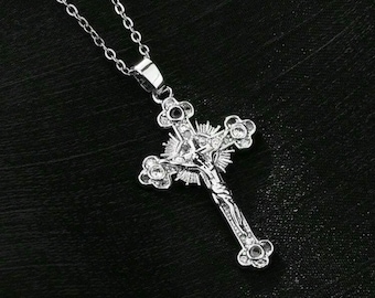 May include: Silver tone cross pendant necklace with a detailed design of a figure on the cross. The cross has small clear stones around the edges.