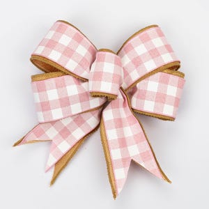 May include: A decorative bow made of pink and white checkered ribbon with gold trim. The bow is tied in a classic style, with multiple loops and tails. The ribbon has a burlap-like texture.