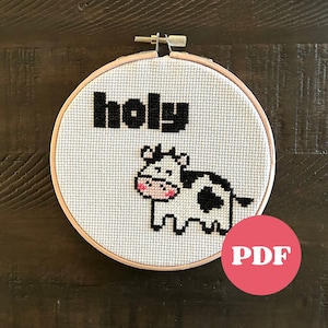 May include: A white embroidery hoop with a black and white cow and the word "holly" stitched in black thread. The hoop is on a brown wooden surface. PDF.