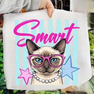 May include: White tote bag featuring a Siamese cat wearing pink glasses and a pearl necklace. The word "Smart" is written in pink above the cat. Light blue vertical stripes and pink and blue stars complete the design.