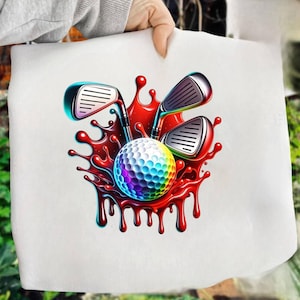 May include: A white tote bag featuring a colorful golf ball and three golf clubs set against a red splash design. The golf ball has a rainbow gradient, and the clubs have silver heads and black shafts. The design is vibrant and eye-catching.