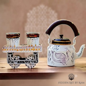 May include: A white metal tea kettle featuring a hand-painted peacock design and a dark brown handle, accompanied by a matching white metal cart stand holding two glass tumblers, both decorated with intricate black and gold painted patterns.