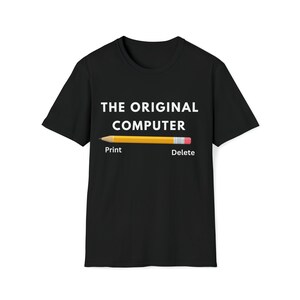 May include: Black t-shirt with the text "THE ORIGINAL COMPUTER" in white. A yellow pencil graphic is centered below the text, with "Print" and "Delete" written on either side of the pencil.