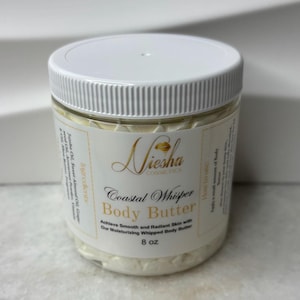 Peut inclure: Un pot en plastique transparent avec un couvercle blanc, rempli de beurre corporel crémeux. L'étiquette indique "Niesha Cosmetics Coastal Whisper Body Butter" et énumère les ingrédients. Le pot contient 227g de produit.