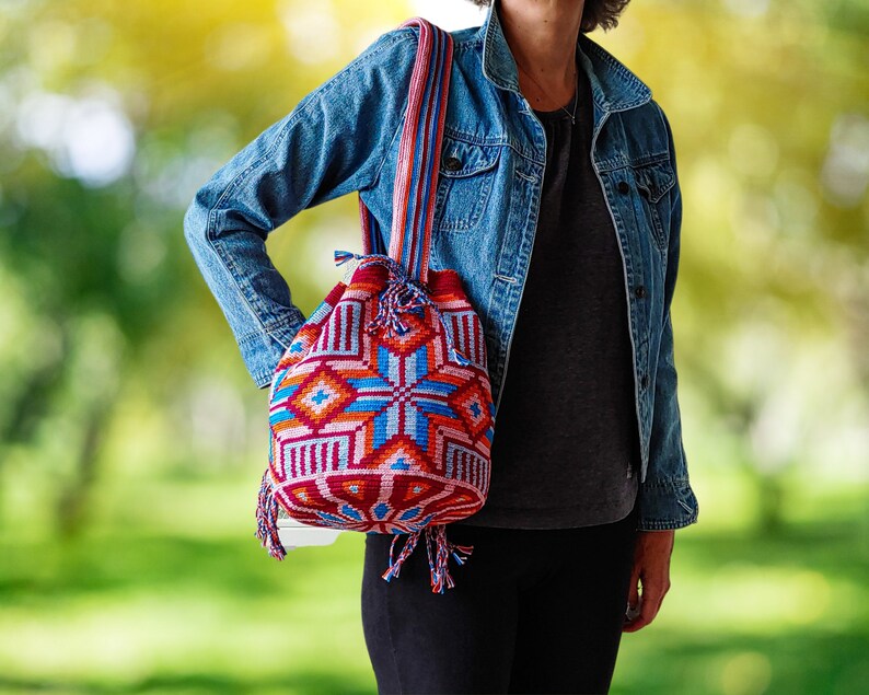 Woman carrying a Wayuu style bag in bright colors turquoise, orange, pink, red, blue with a geometric pattern and a striped carrying strap.