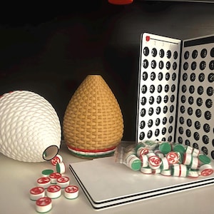 以下が含まれることがあります： ビンゴゲームのセット。ボールが入ったケージ、スコアカード、チップが含まれています。ケージは茶色と白、スコアカードは黒と白、チップは赤、白、緑です。