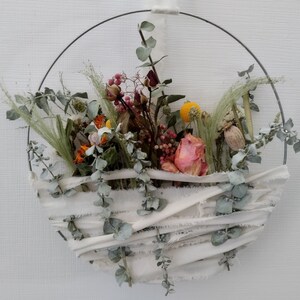May include: A dried flower wreath with a white fabric base and a metal ring. The wreath features dried roses, eucalyptus, and other dried flowers in shades of pink, white, yellow, and green.