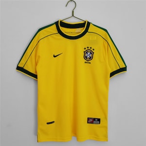 May include: Yellow football shirt with green trim and the Brazilian national team logo. The logo features a blue circle with a white star and the text "BRASIL". The shirt has a Nike swoosh logo on the left chest and a size "M" tag on the bottom right.