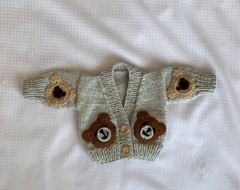 May include: A gray knitted cardigan with brown bear appliques on the front and sleeves. The cardigan has a V-neck and button closure.