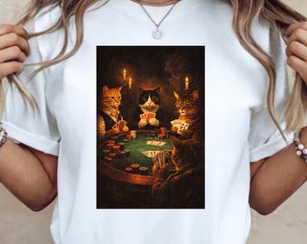 May include: White t-shirt featuring a framed image of cats playing poker. The image shows four cats around a green poker table with cards and chips. The cats are wearing vests and suits, with lit candles in the background.