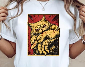 May include: White t-shirt featuring a graphic of an angry yellow cat biting a hand. The cat has red eyes and is set against a red background with yellow accents. The design has a vintage, comic book style.