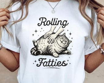 May include: White t-shirt with a graphic of a smiling cat being massaged. The text "Rolling Fatties" is above and below the cat illustration in a distressed font. The design includes star accents.