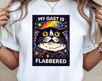 May include: White t-shirt featuring a graphic of a surprised black and white cat with yellow eyes, a rainbow, and the text "MY GAST IS FLABBERED". The cat is wearing a cape with stars.