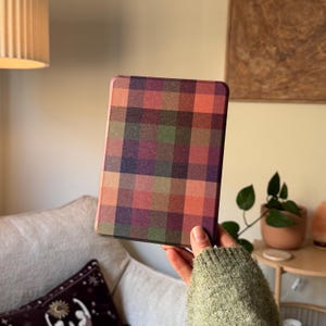 Puede incluir: Un dispositivo lector electrónico rectangular que presenta un vibrante patrón de cuadros multicolor en su superficie frontal. El diseño consiste en una cuadrícula de cuadrados en tonos rojo intenso, verde bosque, naranja apagado y morado oscuro.