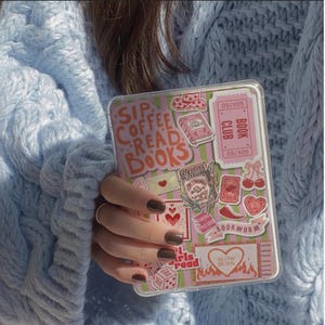 May include: Clear phone case with pink and green striped background and sticker graphics. Stickers include text "SIP COFFEE READ BOOKS", hearts, books, and the words "BOOK CLUB" and "BOOKWORM".