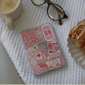 May include: A clear phone case with a pink and green striped background, covered in stickers with book-themed designs and text. The stickers include phrases like "Sip Coffee Read Books" and "Bookworm."