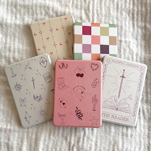 May include: Five rectangular coasters with various designs. One has a pink background with cowboy-themed illustrations. Another features a checkerboard pattern. Others have cherry, celestial, and sword designs. These decorative coasters are ideal for home decor.