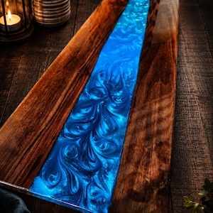 May include: A rectangular wooden serving board with a vibrant blue resin river design. The wood has a rich, dark brown color, and the resin features swirling patterns. This decorative board is ideal for serving appetizers or as a unique home decor piece.