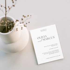 Puede incluir: Una tarjeta de invitaci&oacute;n de boda blanca con texto negro. La tarjeta dice "Juntos con sus familias, Olivia y Marcus, los invitan a compartir su d&iacute;a de boda, s&aacute;bado 16.10.2023, a las cuatro de la tarde, The Stony Avenue Bar & Lounge, Melbourne Australia, Recepci&oacute;n formal a continuaci&oacute;n."