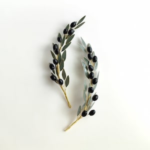 Puede incluir: Dos pinzas para el pelo de rama de olivo doradas con aceitunas negras y hojas verdes.