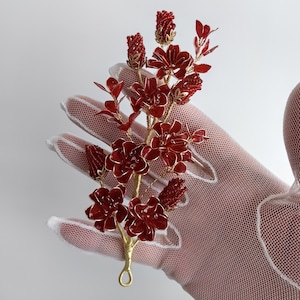 Puede incluir: Un peine de pelo floral de alambre dorado con flores de cuentas rojas. El peine está en un guante de encaje blanco.