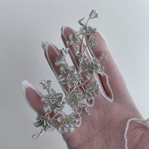 Op de afbeelding: Een zilveren bloemenhaar kam met delicate, ingewikkelde details. De kam is gemaakt van metaal en heeft een cluster van kleine, zilveren bloemen.