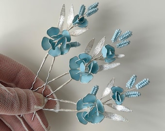 May include: A collection of delicate hair pins featuring light blue flower and bead accents. The floral elements are paired with silver-colored leaves and stems. These decorative hair accessories are ideal for weddings or special occasions.